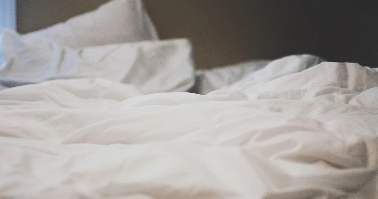 Lençóis brancos e travesseiros sobre uma cama, ilustrando como limpar o colchão